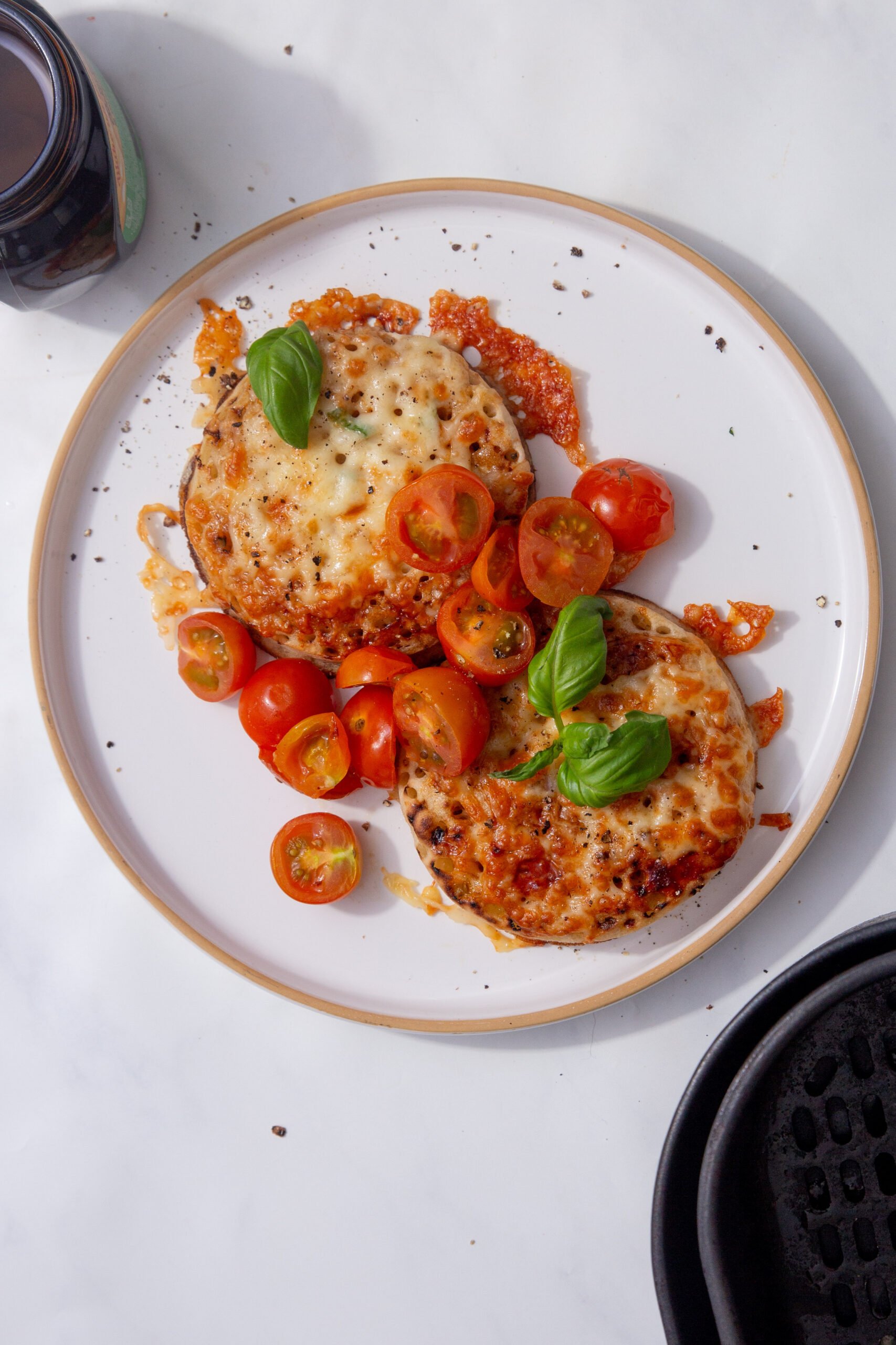 Picture of air fryer crumpets with melted cheese, marmite, and topped with cherry tomatoes and basil leaves.