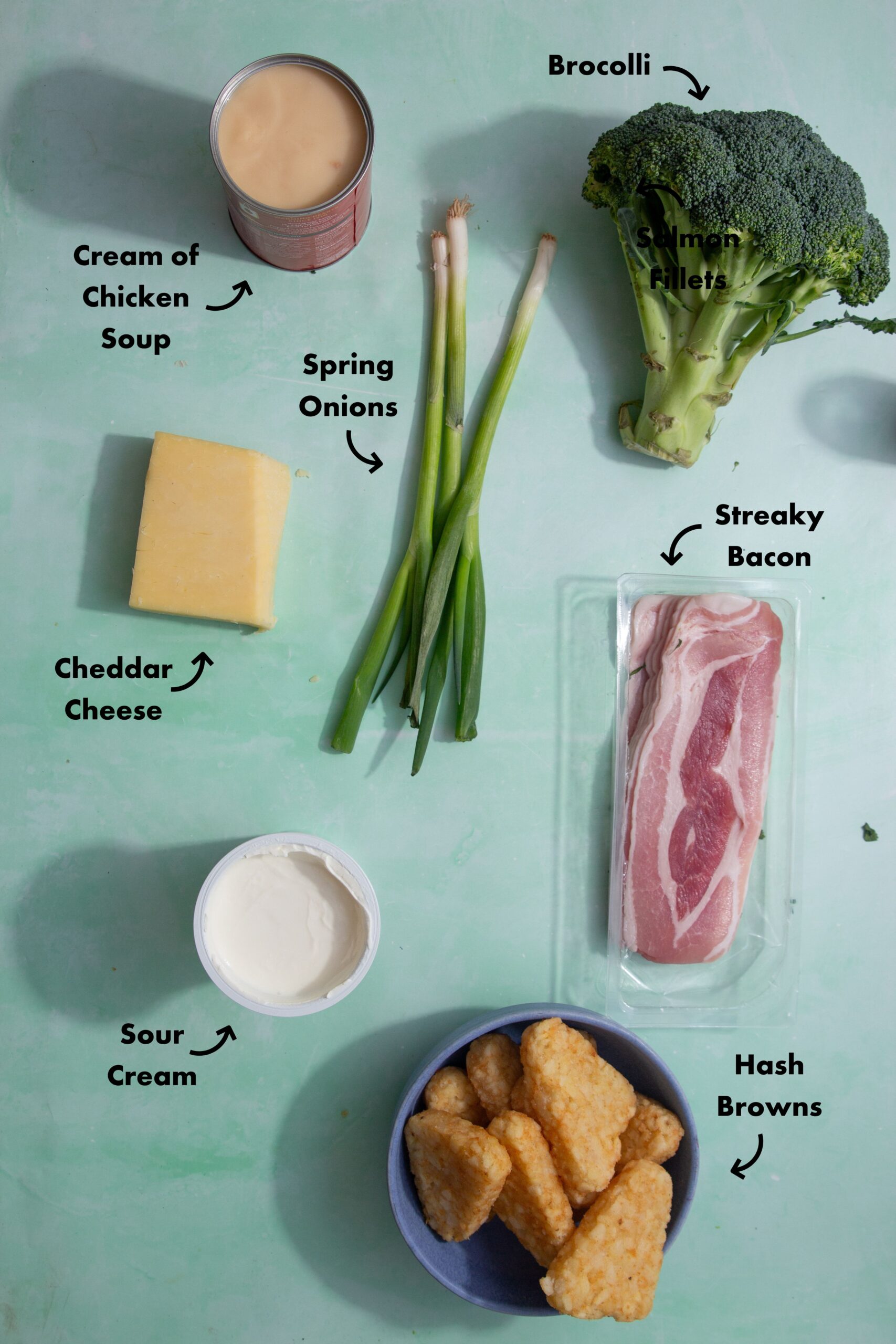 Ingredients to make the hash brown potato soup on the stovetop laid out on a pale blue background and labeled with arrows.
