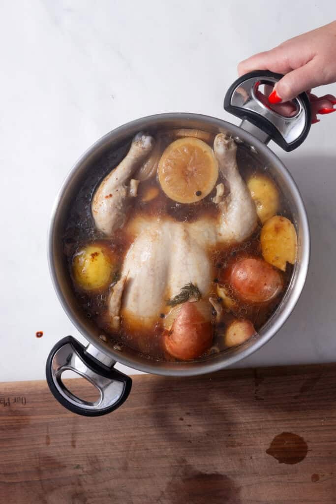 A whole boiled chicken cooked through in a pot.
