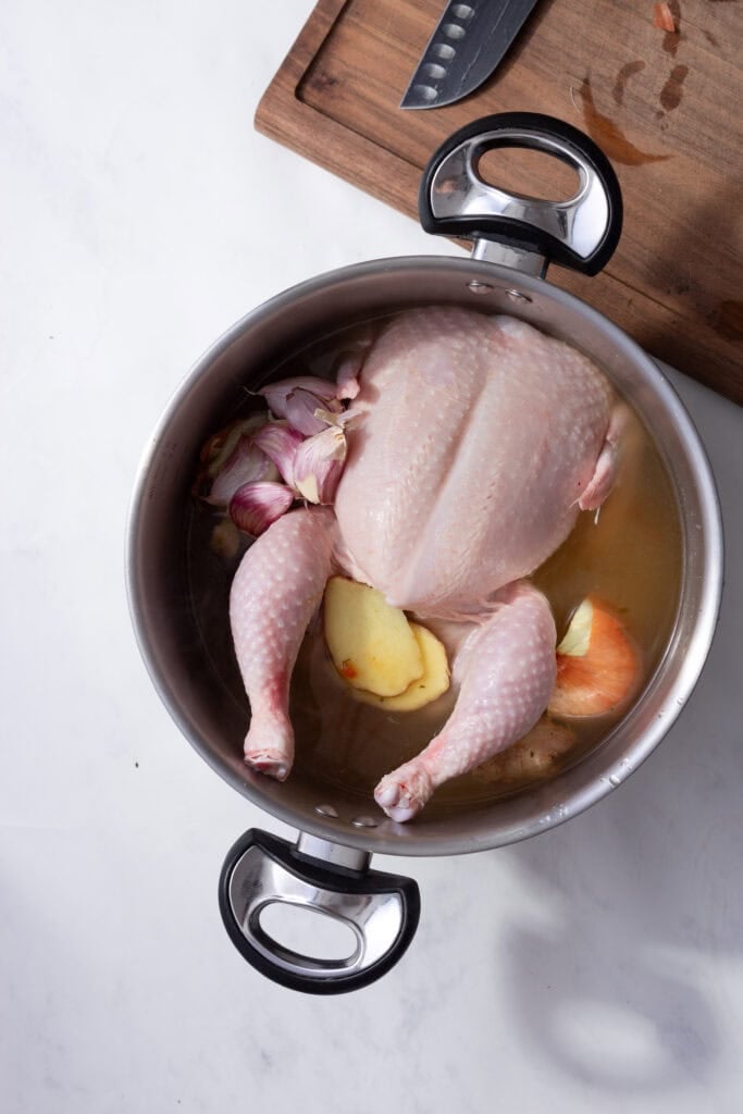 A whole chicken in a stock pot with ginger and garlic cloves.
