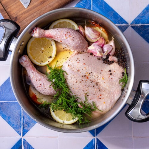 whole chicken in a boiling pot with parsley, garlic, and lemon slices