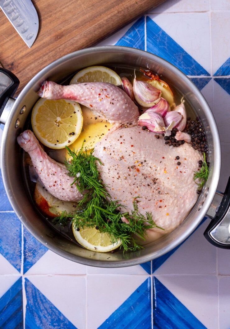 whole chicken in a boiling pot with parsley, garlic, and lemon slices