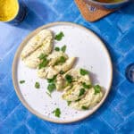 boiled chicken tenderloins on a white plate one a blue background and sprinkled with parsley and black pepper