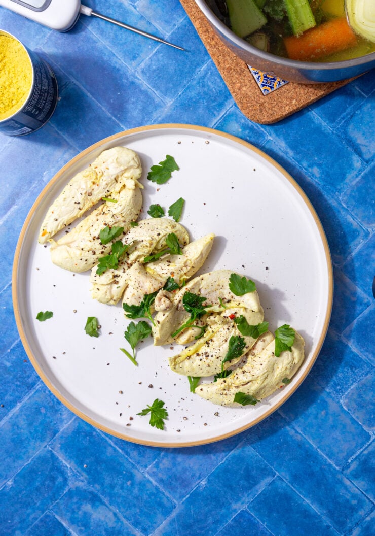 boiled chicken tenderloins on a white plate one a blue background and sprinkled with parsley and black pepper