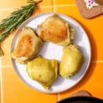 four boiled chicken thighs on a white plate set on an orange tile background
