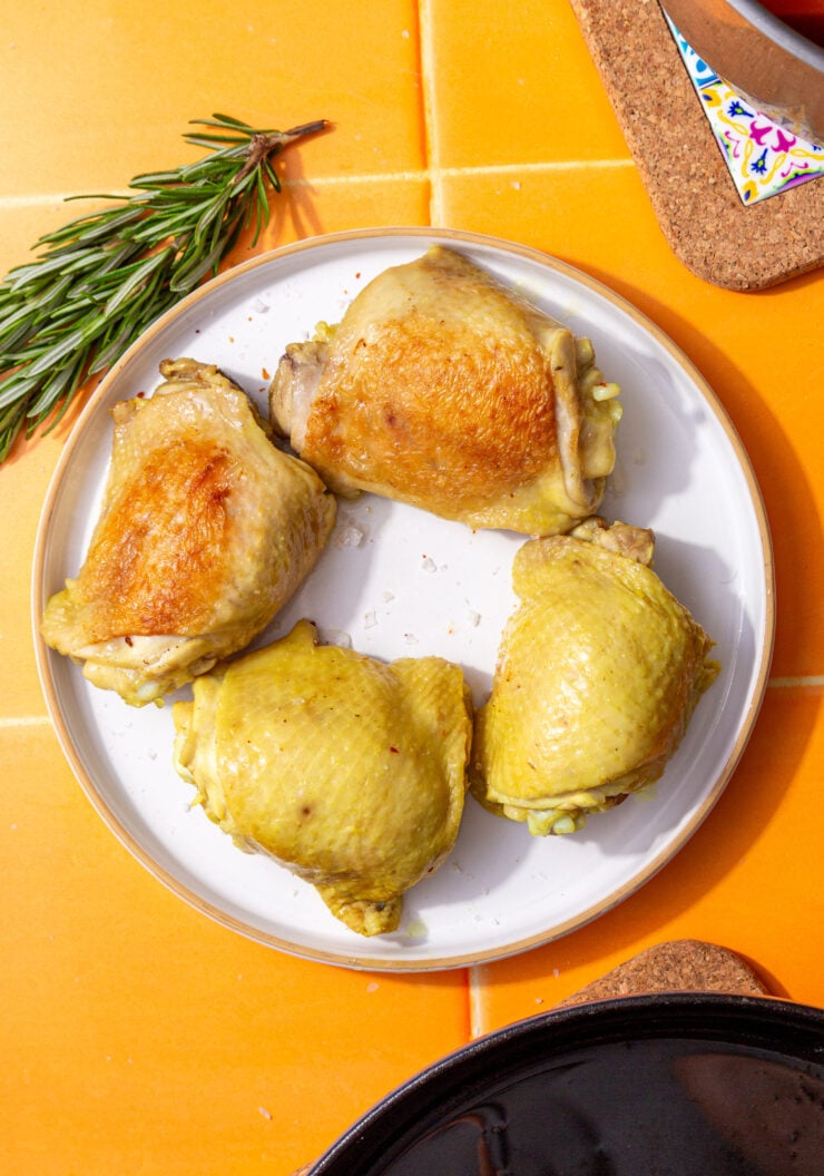 four boiled chicken thighs on a white plate set on an orange tile background