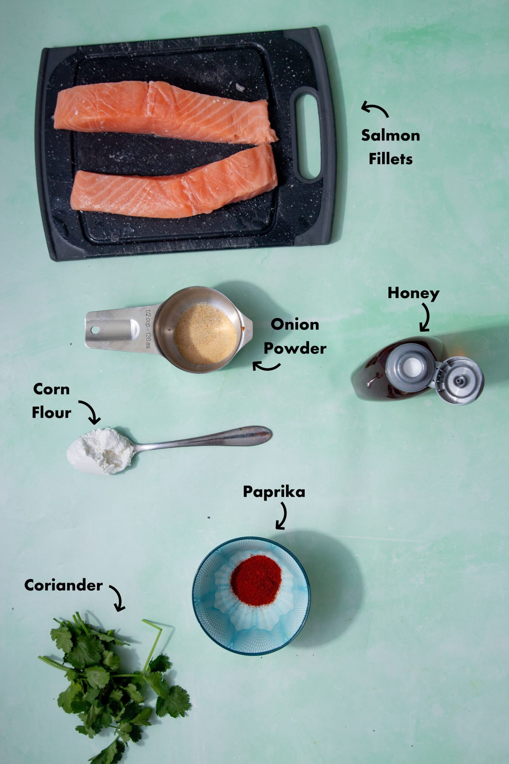 Ingredients to make the pan fried salmon bites laid out on a pale blue background and labeled with arrows