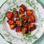 fully cooked pan-fried salmon bites on a green and white plate and sprinkled with spring onions