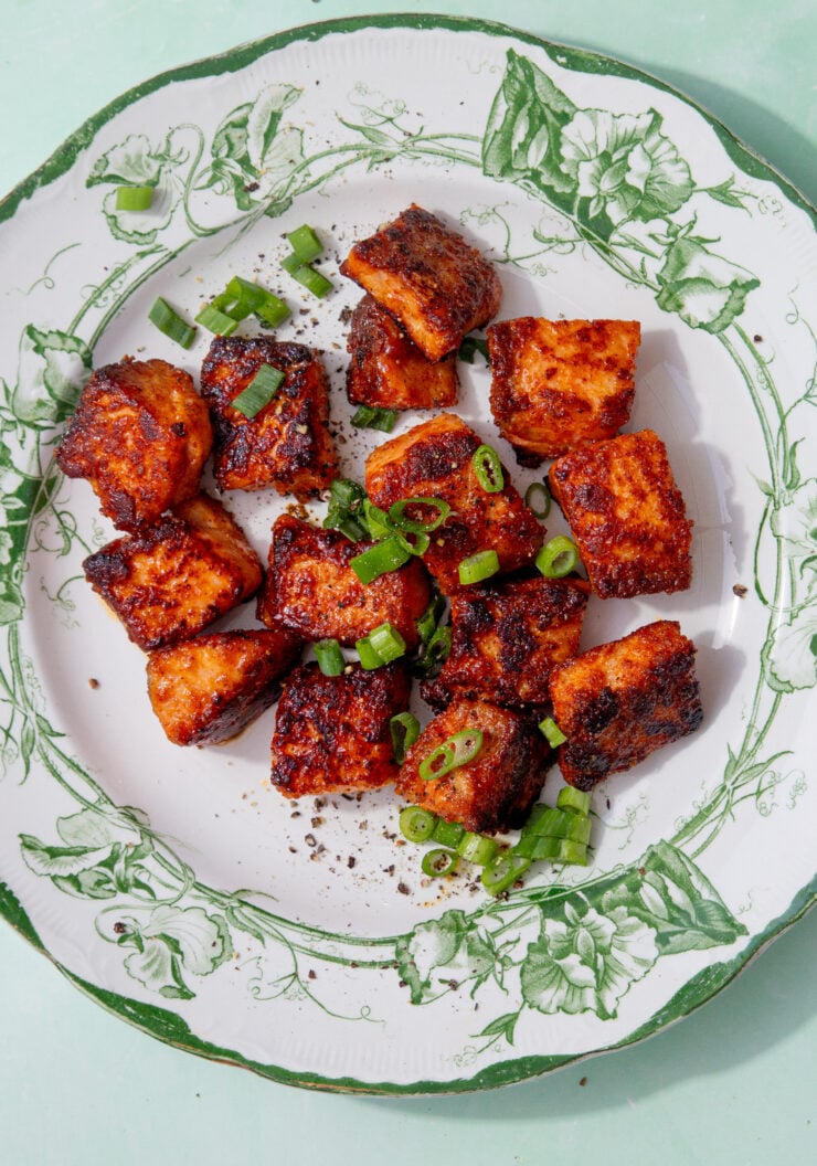 fully cooked pan-fried salmon bites on a green and white plate and sprinkled with spring onions
