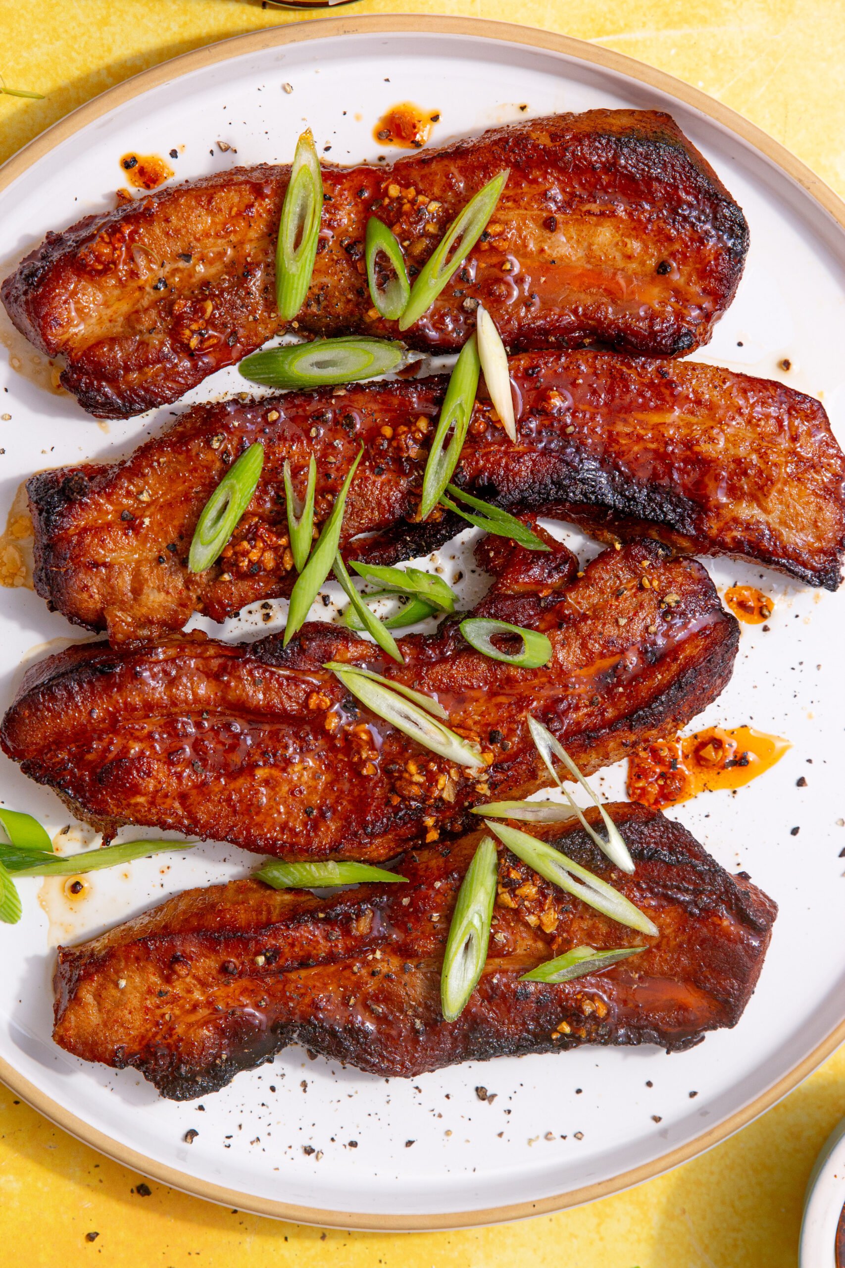 close up image of the air fryer pork belly strips on a white plate with spring onion slices on top