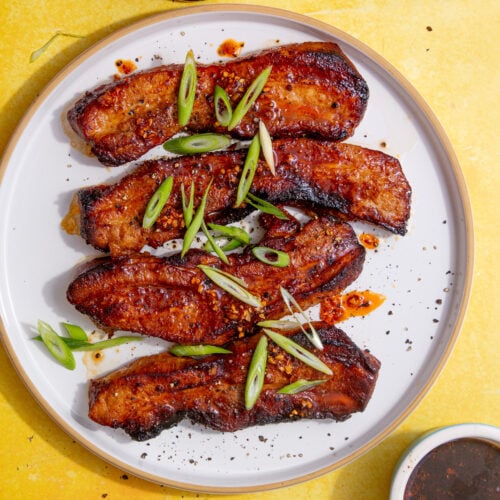 fully air fried pork belly strips on a white plate on a yellow backgorund