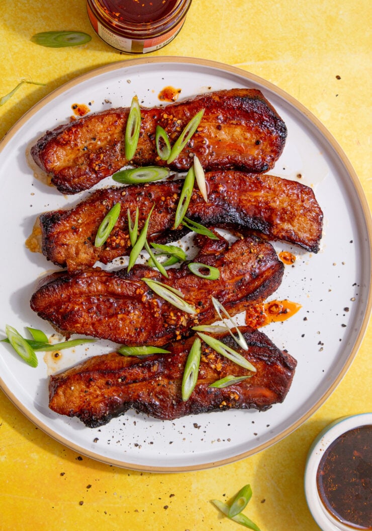 fully air fried pork belly strips on a white plate on a yellow backgorund