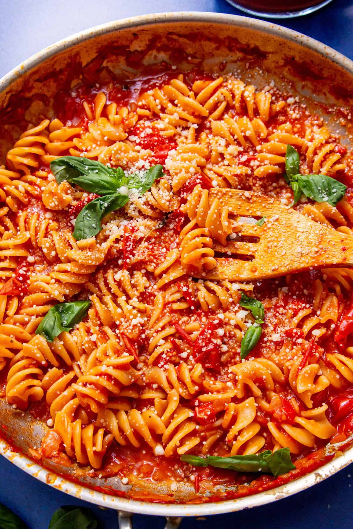 Up close image of spiral pasta covered in red sauce and garnished with white parmesan cheese and green basil leaves with a spoon in the center.