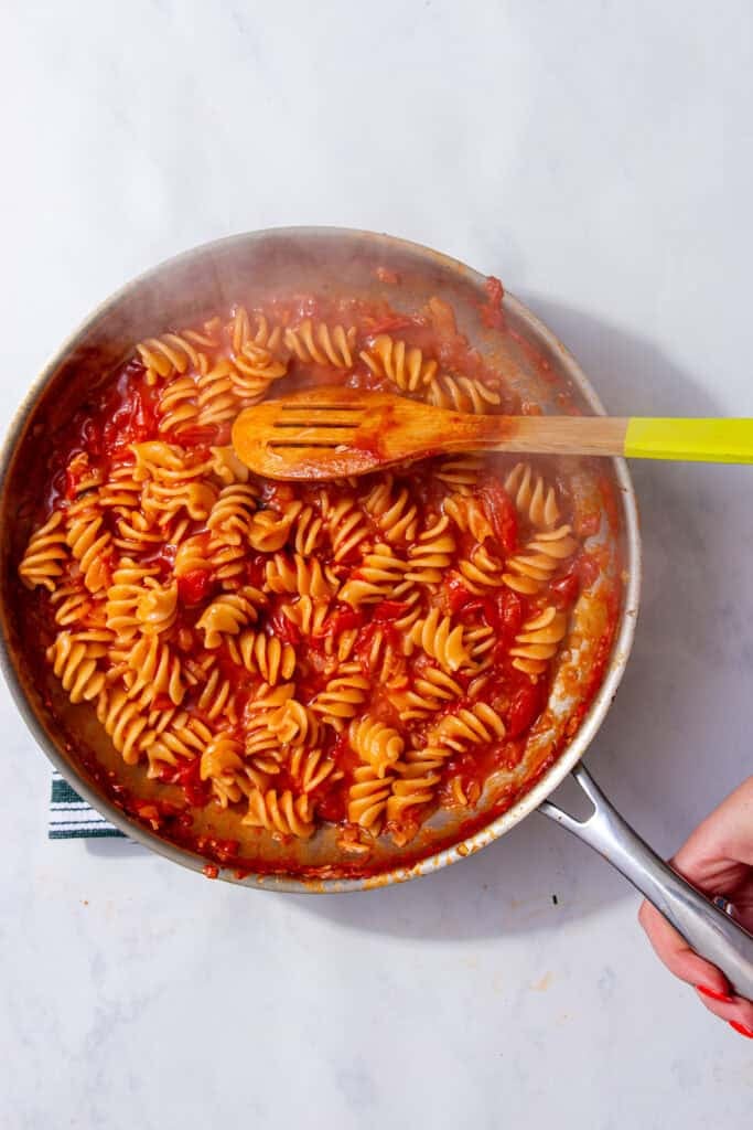 A pan with spiral pasta covered in red sauce and a spoon with a yellow handle.