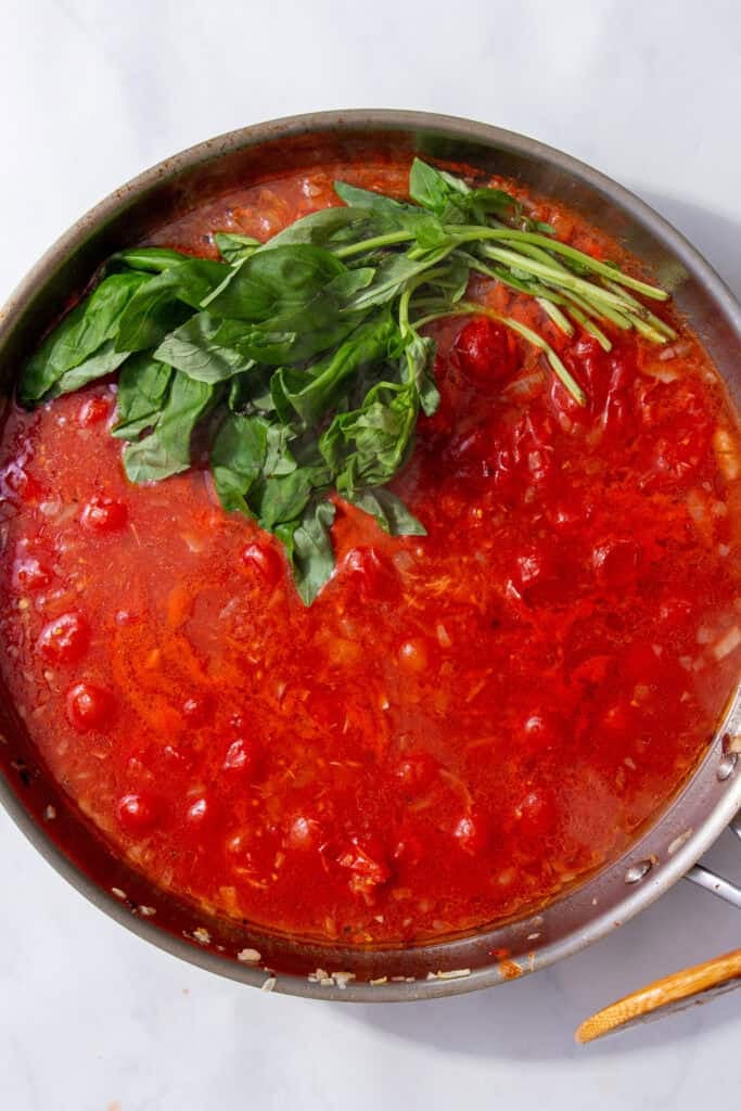 A red sauce in a silver pan with a bunch of green basil in the sauce.