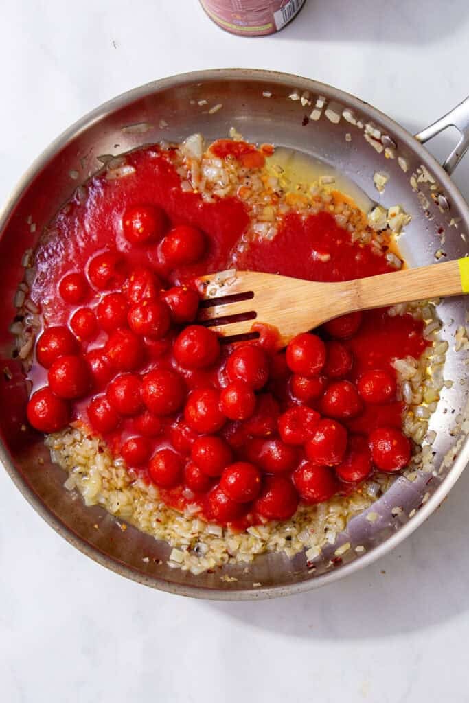 A silver pan with cherry tomatoes, tan sauteed onions and a tan spoon.