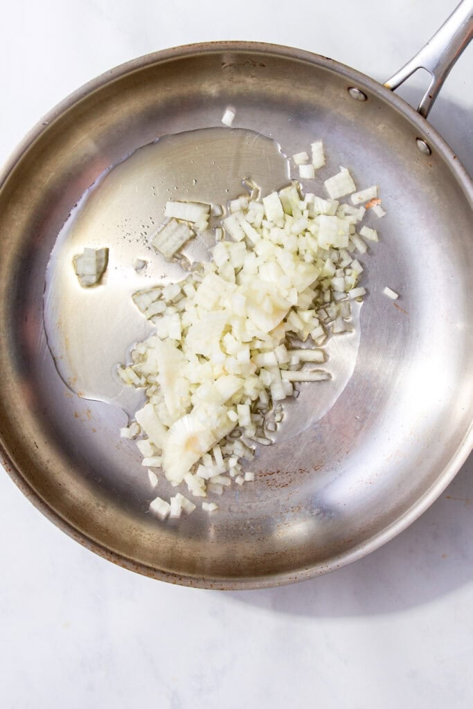 Chopped white onions and oili in a silver skillet.
