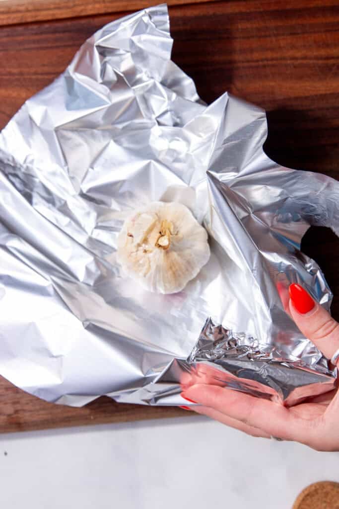 A head of garlic being placed in aluminum foil.