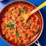 red sauce and spiral noodles in silver pan with a wooden spoon sticking out.