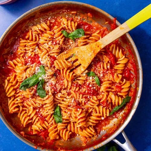 red sauce and spiral noodles in silver pan with a wooden spoon sticking out.