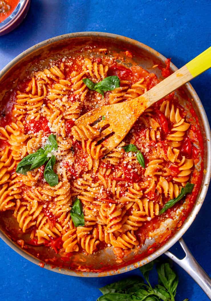 red sauce and spiral noodles in silver pan with a wooden spoon sticking out.