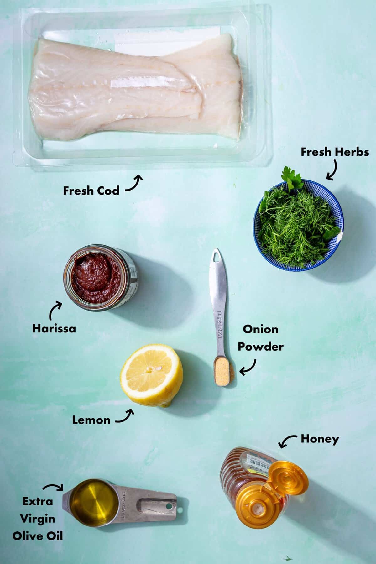 Ingredients to make the air fryer cod laid out on a pale blue background and labeled with arrows.
