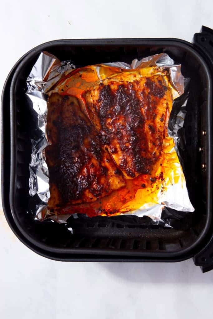 Fully cooked cod fillets with brown seasoning paste in a foil lined air fryer basket.