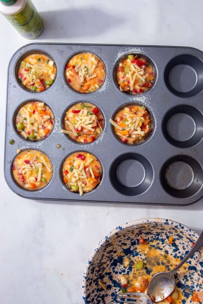 Colorful mixture of vegetables and eggs sprinkled with shredded cheese in a grey muffin tin.