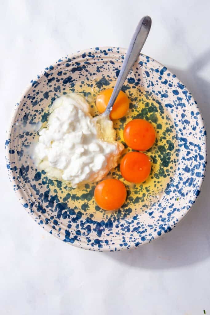 Four eggs and white cottage cheese in a blue and white speckled bowl.