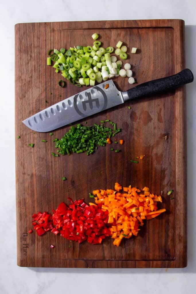 Chopped vegetables on a brown cutting board next to a silver knife.