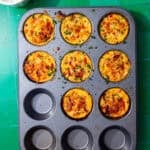 Yellow egg bites with cottage cheese in a grey muffin tin, sprinkled with chopped chives.