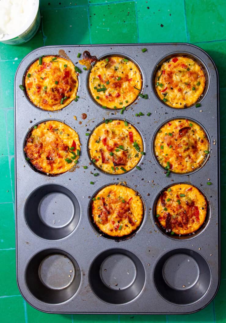 Yellow egg bites with cottage cheese in a grey muffin tin, sprinkled with chopped chives.