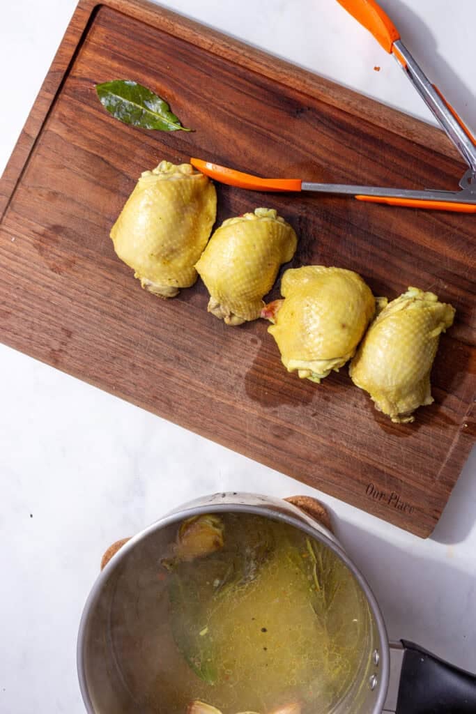 Four fully boiled chicken thighs resting on a cutting board. 