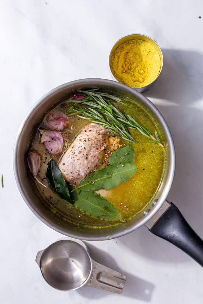 Rosemary sprigs, garlic cloves, and bay leaves in the saucepan with the chicken thighs and broth.