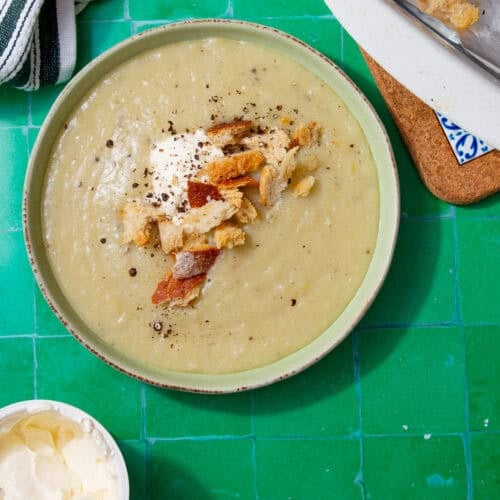 Tan soup topped with white cream and croutons on a green background.