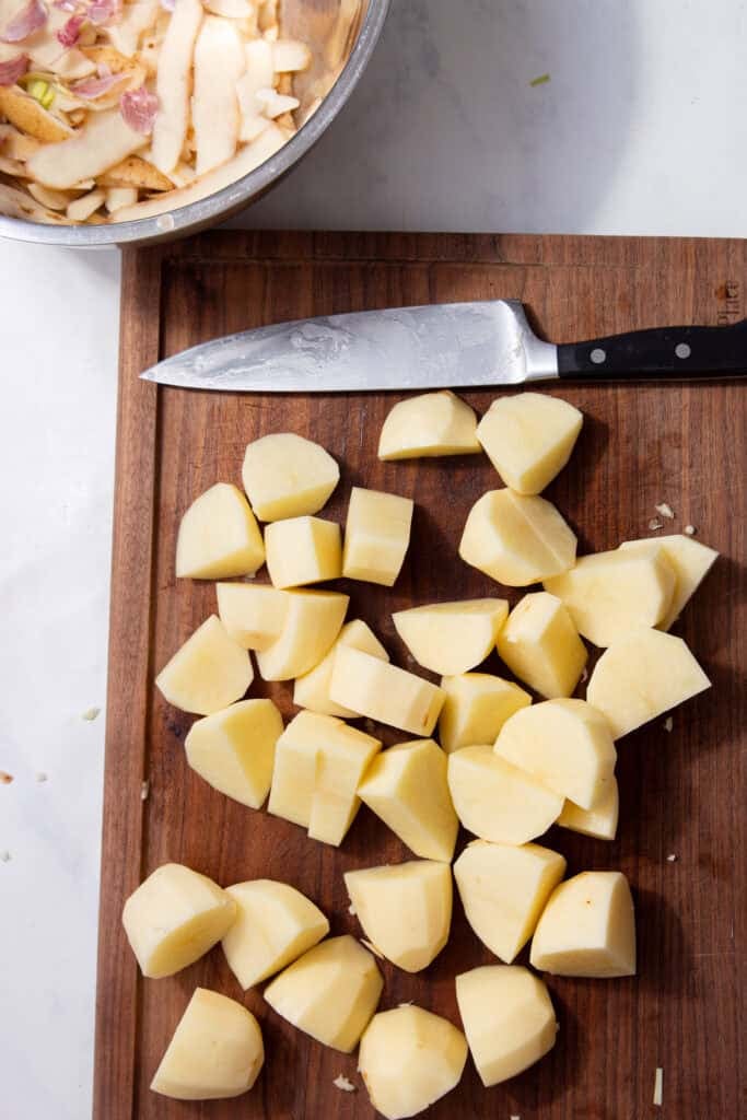 Cut up potatoes on a cutting board laying next to a large silver and black knife.