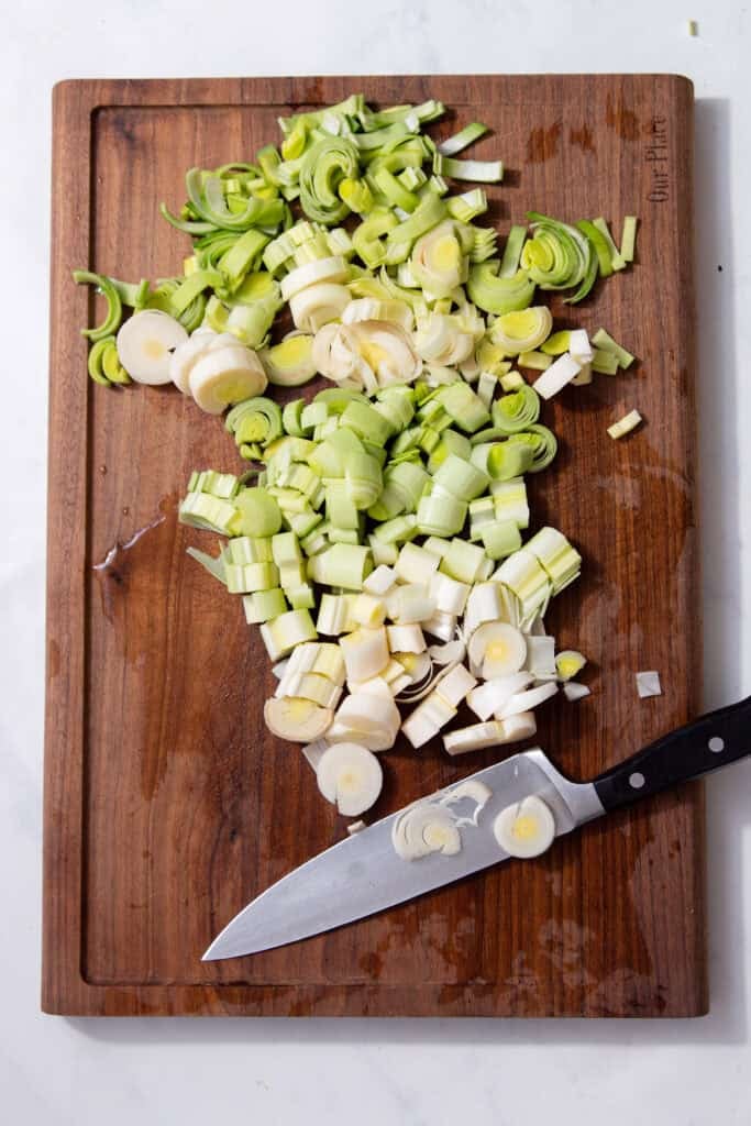 Green leeks sliced on a cutting board next to a large silver and black knife.