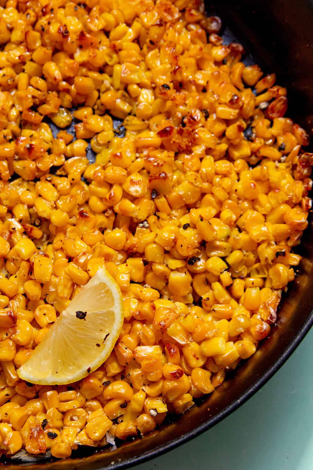 Close up image of roasted corn on a black background and garnished with a yellow lemon wedge.