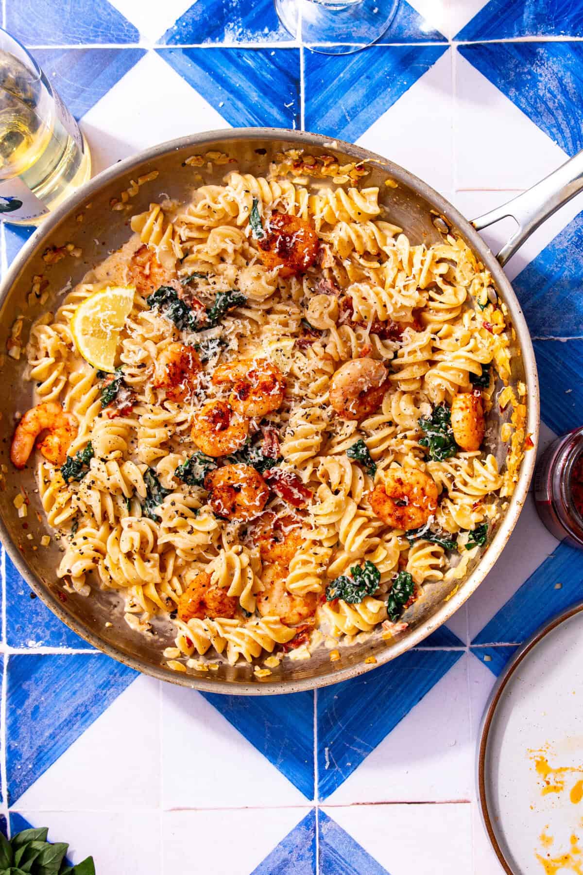 One-pan Marry Me Shrimp Pasta served family-style on a blue and white tiled table, topped with parmesan, shrimp, and lemon.
