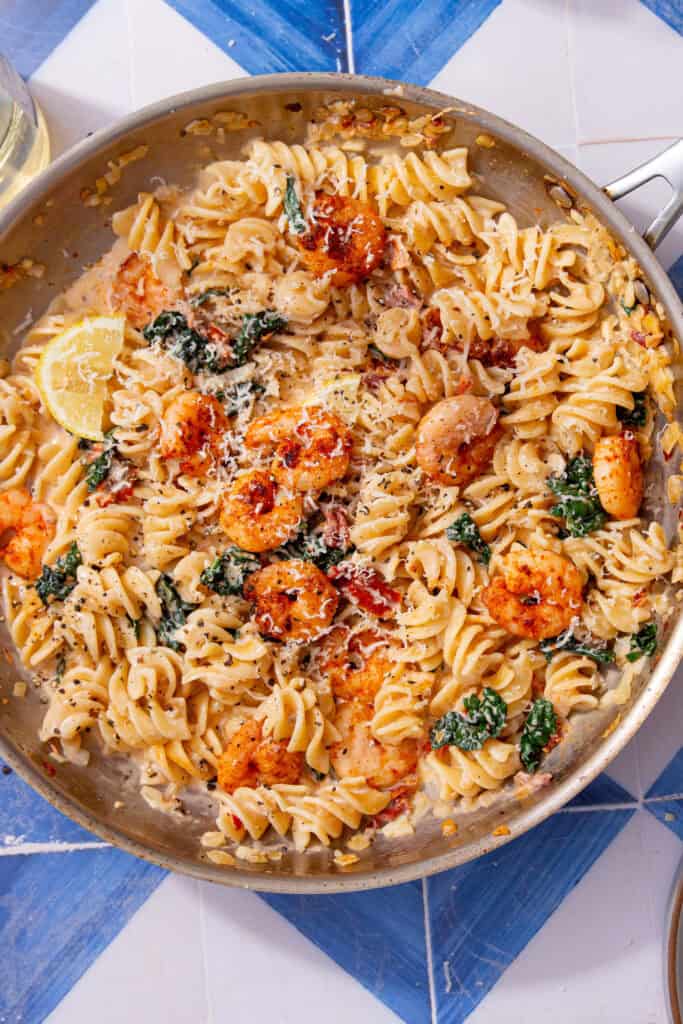 Finished Marry Me Shrimp Pasta dish in the pan, topped with prawns, grated parmesan, and a wedge of lemon.