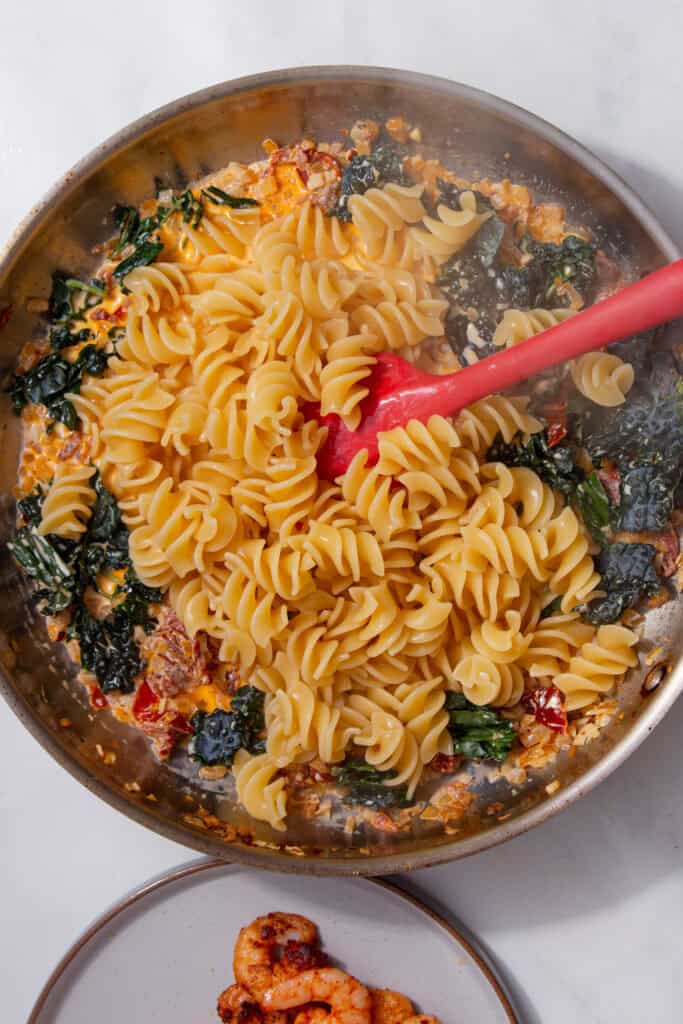 Cooked pasta being added into the creamy sauce with cavolo nero in the pan.