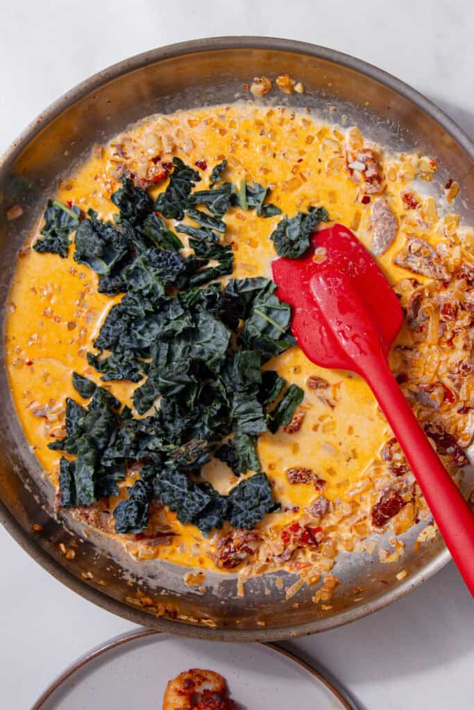 Dark green cavolo nero leaves sitting on top of the creamy sauce before being stirred in.