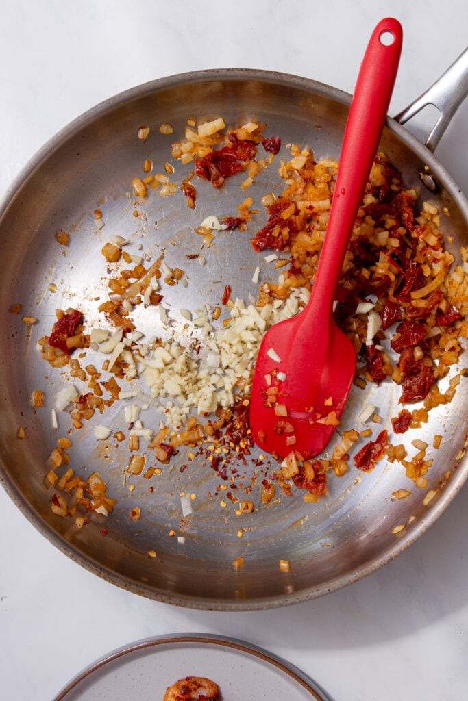 Finely chopped garlic added to softened onions and sun-dried tomatoes in the pan.