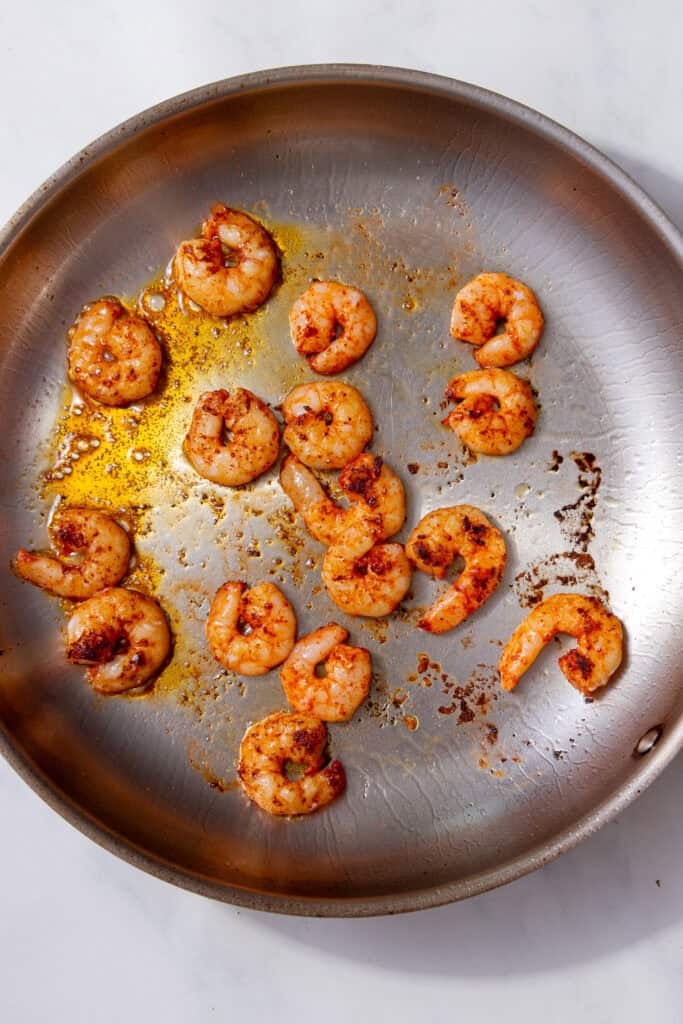 Prawns frying in a pan with a little oil, turning pink and slightly charred.