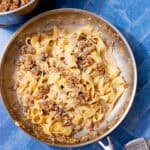 Creamy ragu bianco tossed with fresh pappardelle and topped with grated parmesan and black pepper in a stainless steel pan.