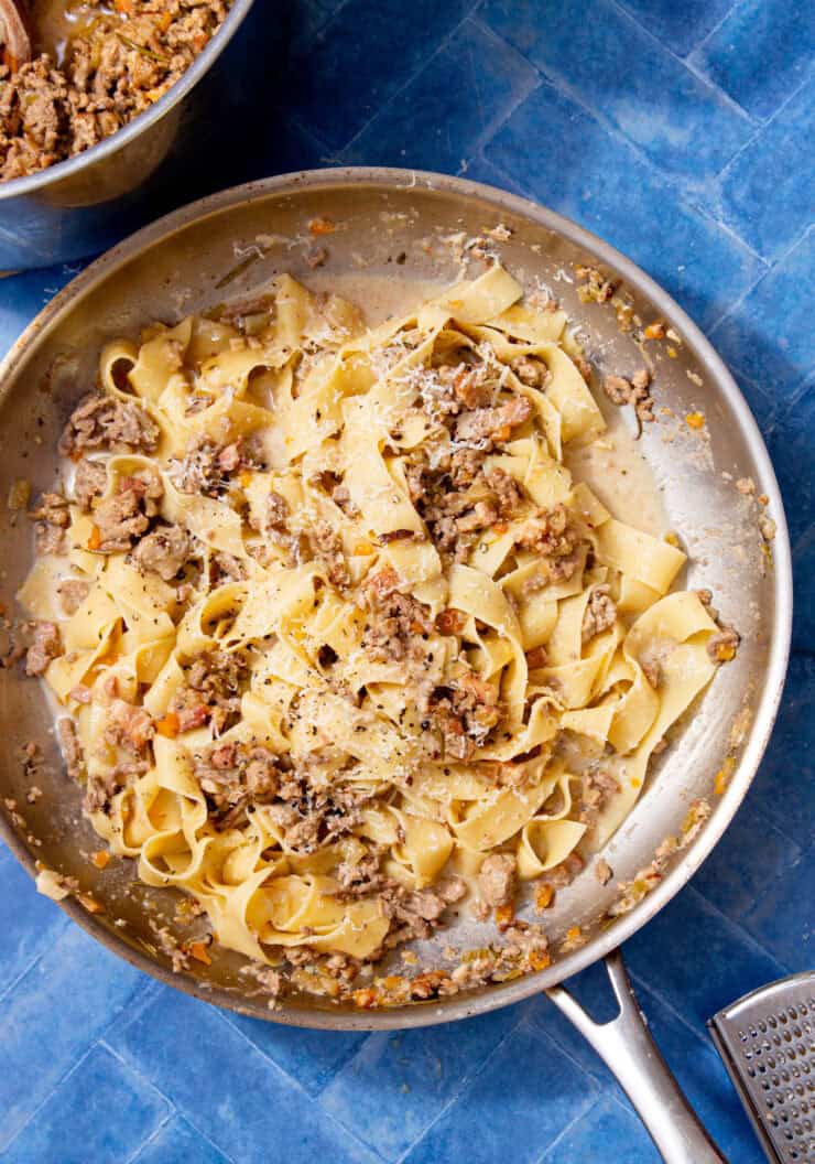 Creamy ragu bianco tossed with fresh pappardelle and topped with grated parmesan and black pepper in a stainless steel pan.