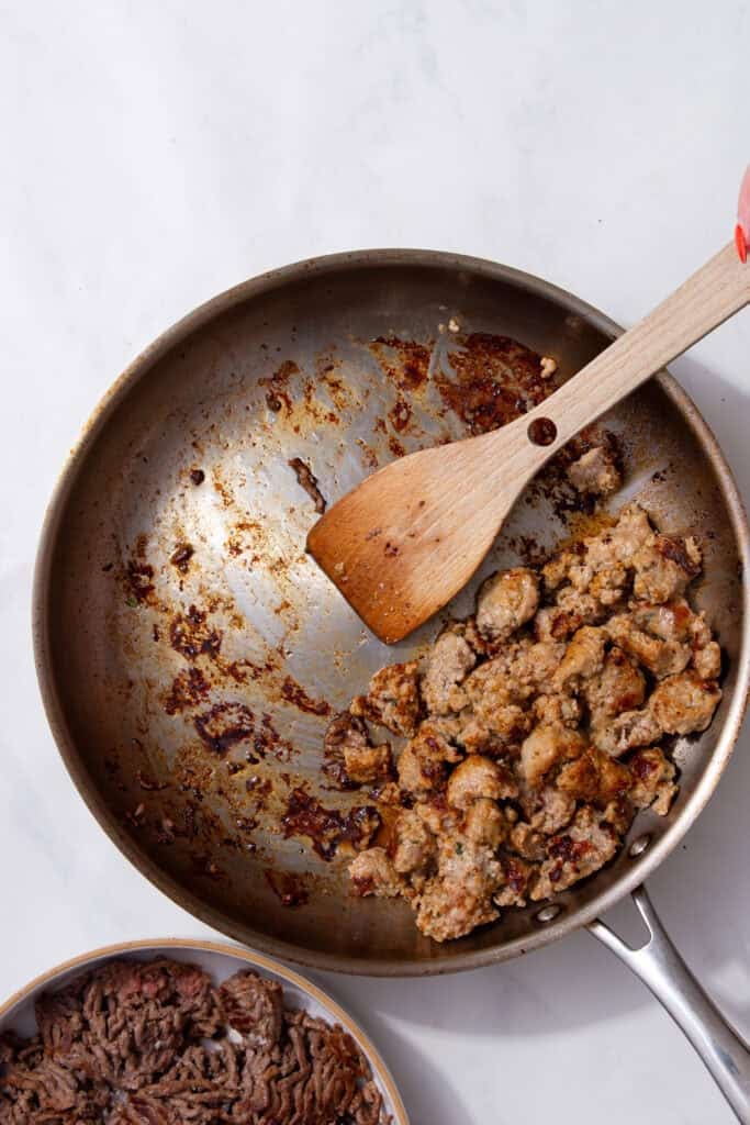 Browned sausage cooking in a pan with seared beef mince set aside.