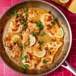 Skillet of easy chicken piccata with golden chicken, capers and lemon wedges.