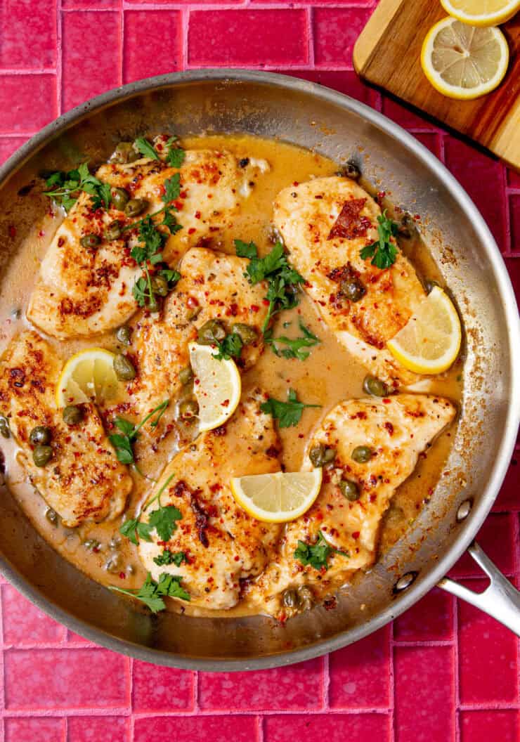 Skillet of easy chicken piccata with golden chicken, capers and lemon wedges.