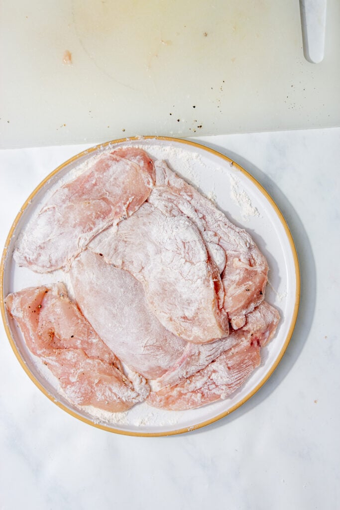 Chicken breasts fully coated in flour on a plate.